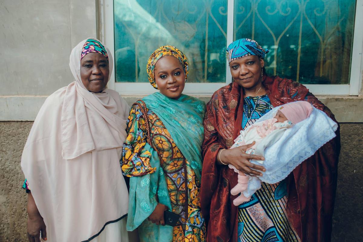 Three Nigerian women in traditional dress, with one holding a baby.